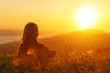 © JenkoAtaman - Woman sits with her back in the field and admires the sunset in the mountains.