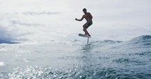 Surfer On Hydrofoil Surfboard Riding Blue Ocean Wave. Futuristic Surfing On Hoverboard