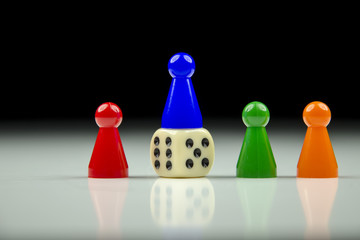 Close-up view of a row of colored figures and playing cube with blurred black and white background with reflection