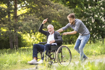 Hipster son walking with disabled father in wheelchair at park.