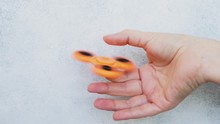 Someones Hand Showing Trick With One Orange Fidget Spinner On Light Gray Background, Popular Relaxing Toy, Generic Design