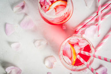 Summer Refreshment Drinks. Light Pink Rose Cocktail, With Rose Wine, Tea Rose Petals, Lemon. On A White Stone Concrete Table. With Striped Pink Tubules, Petals And Rose Flowers. Copy Space Top View