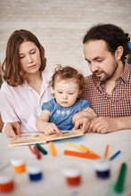 Portrait Of Family Spending Time With Cute Little Daughter, Reading Stories And Painting Together