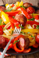 Fettuccine pasta with roasted bell pepper, tomato and sausages close-up. vertical