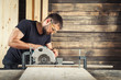 © Виталий Сова - The man builder uses a modern circular   saw in order to saw the board in the workshop