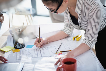 Wall Mural - Young asian businesswoman in eyeglasses working with blueprint in office