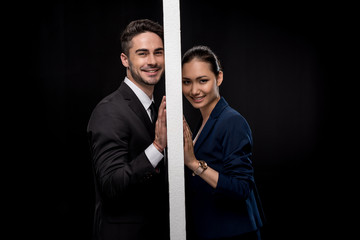 Side view of young smiling couple separated by wall and looking at camera isolated on black