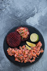 Wall Mural - Above view of a stone slate tray with salmon tartare and beetroot cutlets. Vertical shot on a grey stone background with copyspace