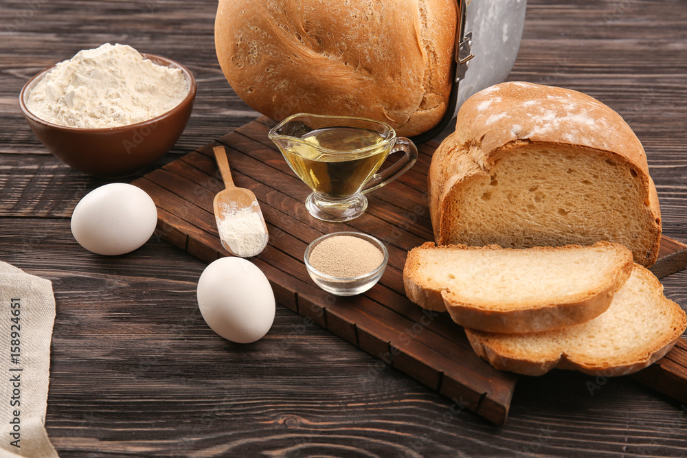 Loaf in bread machine pan and ingredients on wooden table