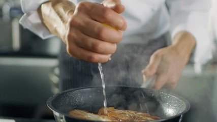 Wall Mural - Professional Chef Squeezes Lemon Juice onto Hot Pan with Red Fish Fillet on it. He Works in a Modern Kitchen. Shot on RED EPIC-W 8K Helium Cinema Camera.