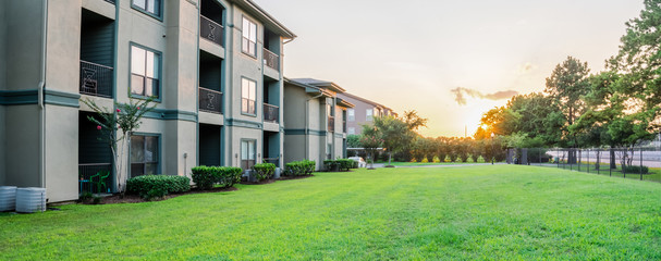 Wall Mural - View from grassy backyard of a typical apartment complex building in suburban area at Humble, Texas, US. Sunset with warm light. Panorama style.