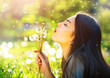 Beautiful young woman blowing dandelions and smiling