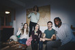 © Maskot - Portrait of cheerful young friends on sofa against world map at college dorm