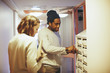 © Maskot - Woman standing by male friend opening mailbox in dorm corridor