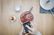 © Maskot - Cropped image of woman using mobile phone over tomato soup at table in dorm