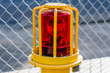 A red rotating emergency light inside a yellow metal cage with chain link fence in the background