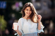 © chichkaua - Close up fashion street style portrait of a beautiful girl in a casual outfit walks in the city . Beautiful brunette Keeps coffee.