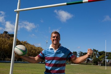 Wall Mural - Portrait of happy rugby player holding ball against blue sky