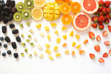 Top View Of Whole Fruits And Cut Slices In The Rows, Red, Orange, Yellow, Green Fruits With Cut Pieces On The White Background, Grapefruit, Mango, Strawberries, Orange, Lemon, Kiwi
