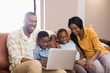 © WavebreakMediaMicro - Happy parents and children using laptop while sitting on sofa