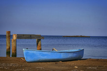 Blue Rowboat Anchored On The Shore Of The Ocean By A Pier