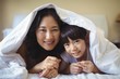 © wavebreak3 - Mother and daughter relaxing under blanket in bedroom