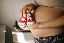 Pregnant Woman Holding Baby Shoes Against Her Belly 