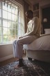 © WavebreakMediaMicro - Full length of thoughtful man sitting on bed by window
