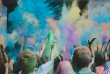 partypeople throwing colorful powder in the air at an outdoor music festival