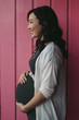 © Rob and Julia Campbell/Stocksy - Pretty young pregnant woman standing near pink wall outside