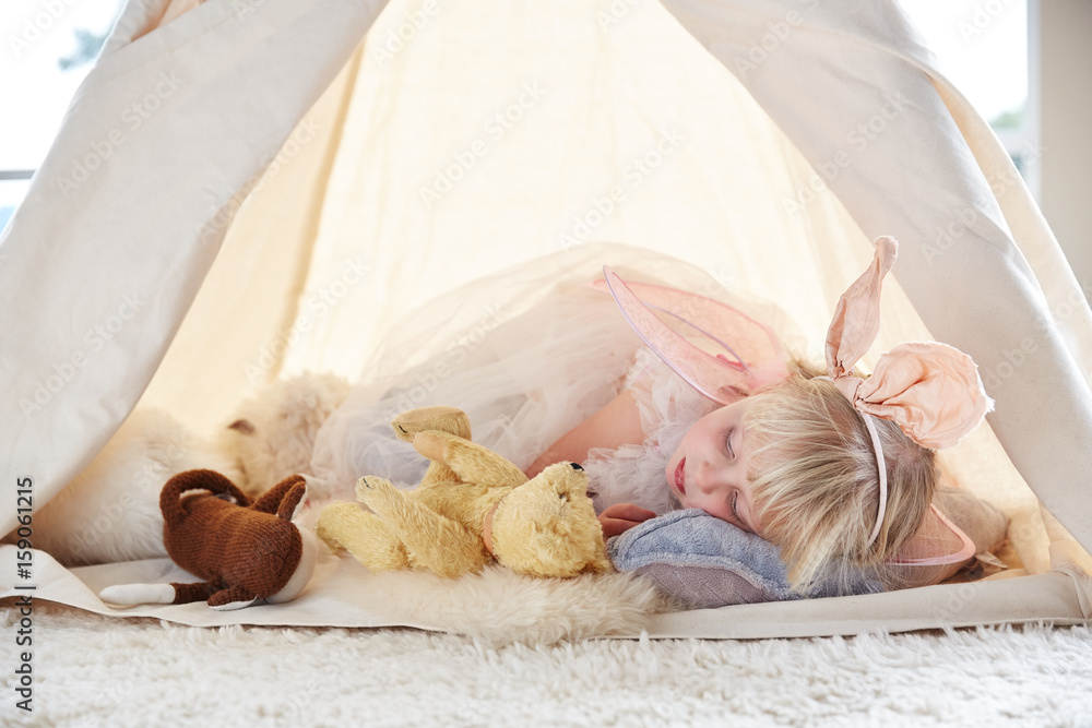 Adorable little girl playing dress up in a teepee tent in living room ...