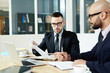 © pressmaster - Two confident men discussing financial documents in office