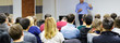 Adult students listen to professor's lecture in small class room. Panoramic aspect ratio.