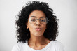 © wayhome.studio  - Black female model with Afro hairstyle and healthy-looking skin wearing big glasses blowing her lips looking curious and funny into camera isolated over white background. People and emotions concept