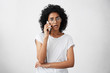© wayhome.studio  - Afro American housewife with curly hair wearing big round glasses and casual T-shirt talking over smartphone with her friend while having free time having surprised look after hearing shocked news