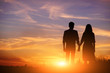 © cezarksv - young couple is holding hands on a background sunset silhouette