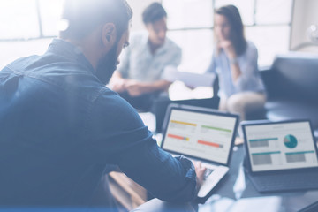 Three partners making research for new business direction.Young businessman working modern laptop and showing documents to young colleague.Business people meeting concept.Blurred background.