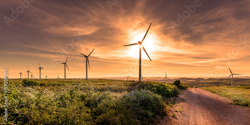Zdjęcie XXL na szczycie wzgórza o zachodzie słońca, polnej drodze i turbinach wiatrowych ustawionych nad krajobrazem w tle