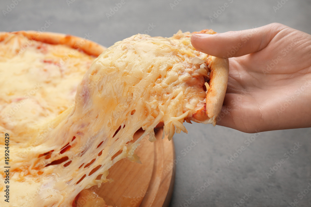 Human hand holding slice of pizza with melted cheese