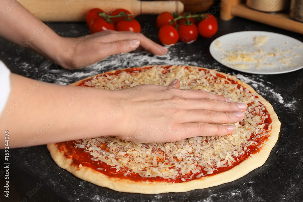 Female chef sprinkling cheese onto uncooked pizza on table