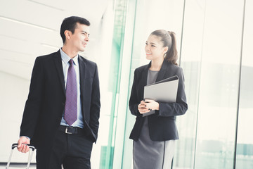 Wall Mural - Businessman walking and pulling luggage handle while talking with a businesswoman