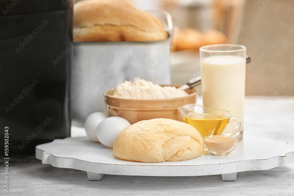 Wooden board with dough and bread machine on table