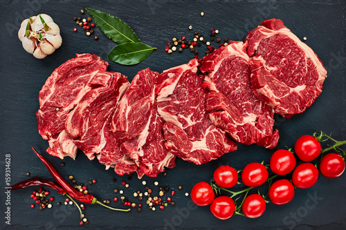 Fotografía Filetes de carne cruda fresca con pimienta y tomates en tablero de pizarra negro