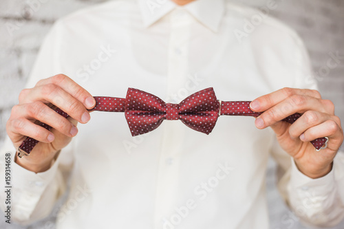 Fotografie, Obraz Closeup of adult stylish handsome man adjusting stylish brown male bow tie while preparing for formal event