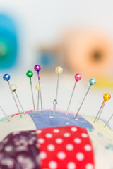 closeup sewing tools, patchwork, tailoring and fashion concept - macro with colorful stitched pincushion and many beautiful pins, background skeins of pink and blue thread, selective focus, vertical