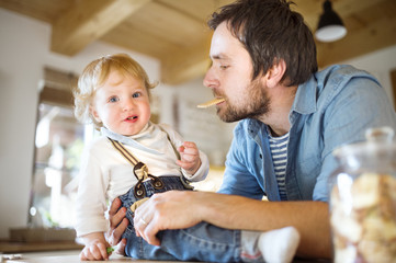 Young father at home with his little son eating biscuit together.