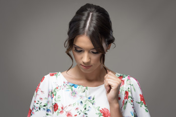 Young elegant woman with bun hairstyle touching hair lock looking down over gray studio background with vignette.