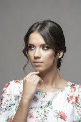 Wall Mural - Vertical portrait of young elegant woman with bun hair thinking and looking away over gray studio background.