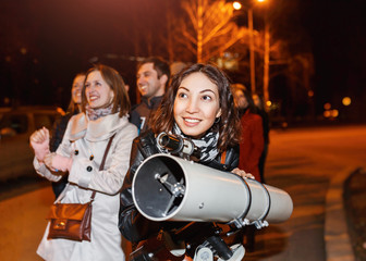 group of people at night looks at the starry sky in a large professional telescope and smiles