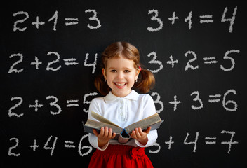 Wall Mural - Happy schoolgirl preschool girl with book near school blackboard